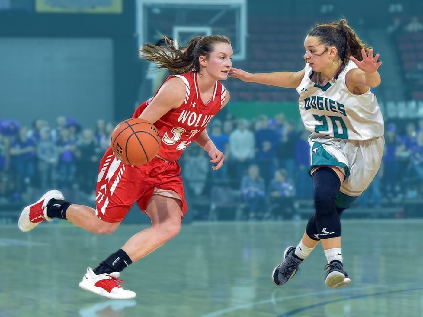Two girls play basketball, one dribbles the ball while wearing a red jersey. The other wears a white and green jersey and attempts to stop the other player.