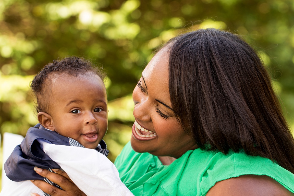 A Black mother holding her baby and smiling.