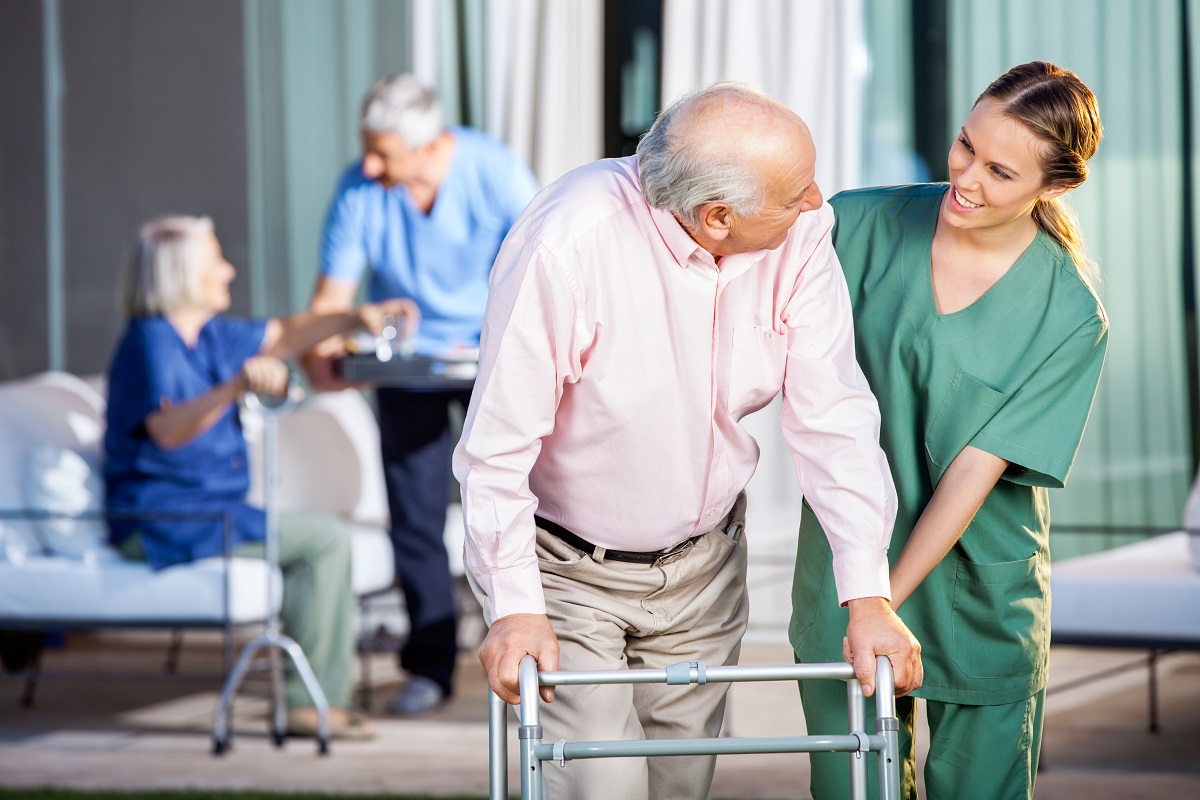 A nurse helps an elderly man with a walker.