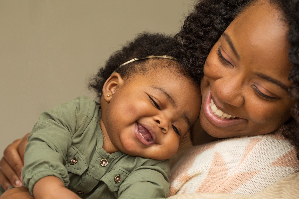 A Black mother holds her baby and smiles