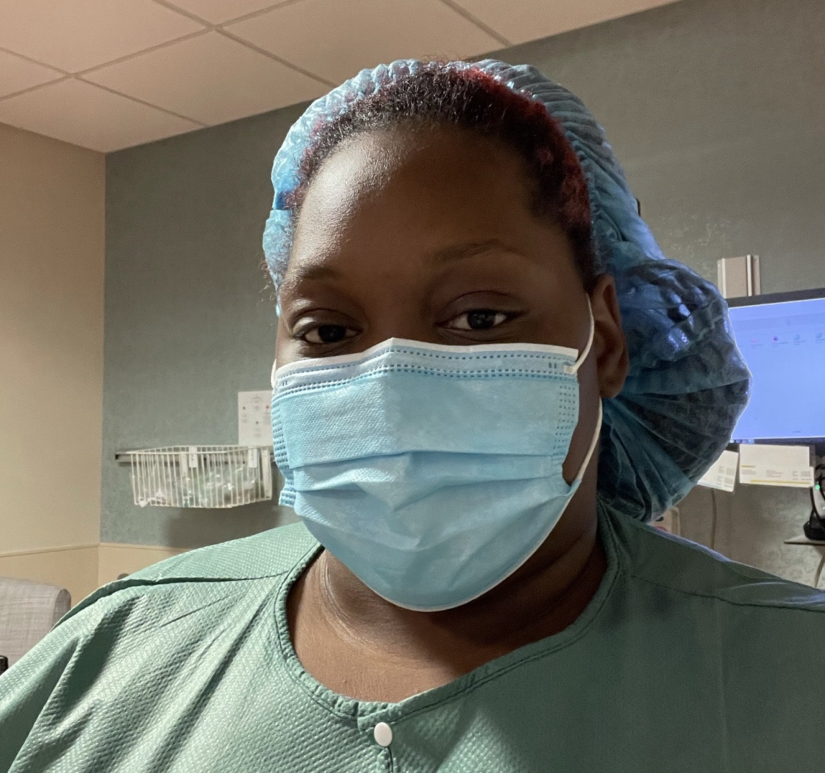 Iyanna Bridges, birth doula and founder of The Birthing Hut wears a mask, scrub cap and scrubs in a delivery room